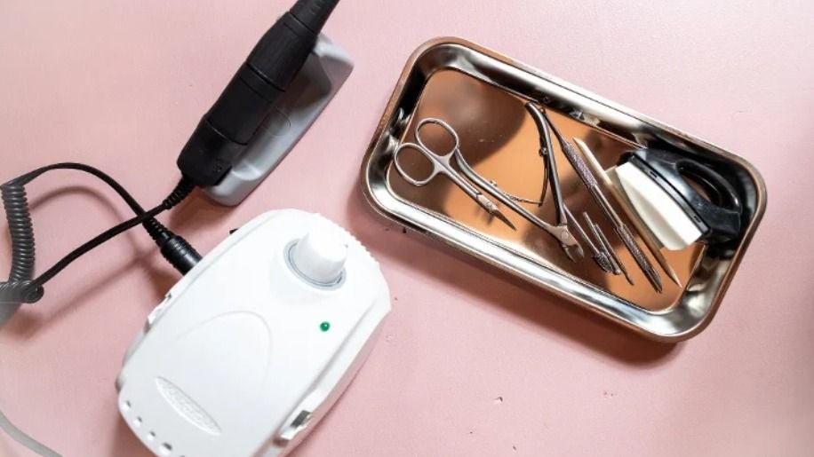 Nagelfrees, schaartjes en instrumenten in een metalen bakje op een roze tafel